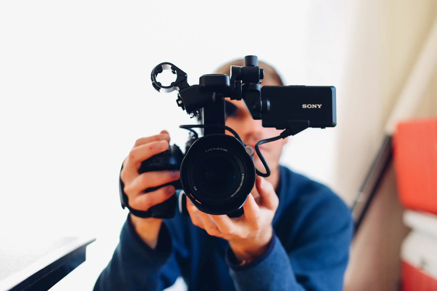 Person holding and filming with a professional Sony video camera focused on the lens indoors.