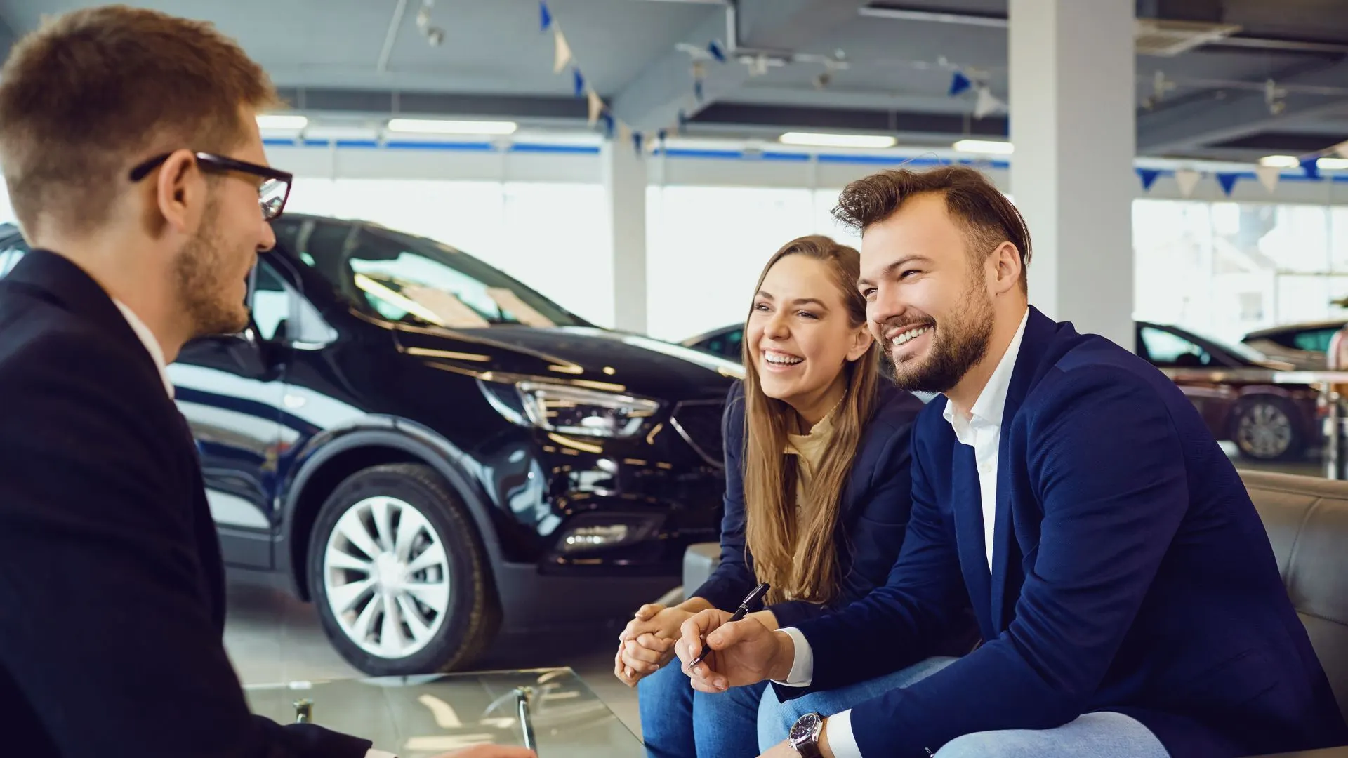 A salesperson talks with a smiling couple in a car showroom