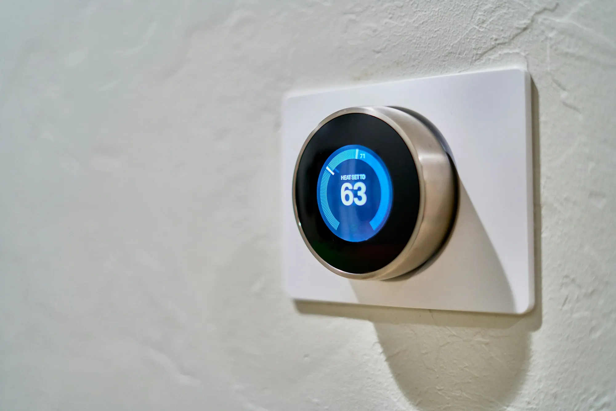 Smart thermostat mounted on a white wall displaying temperature set to 63 degrees Fahrenheit.